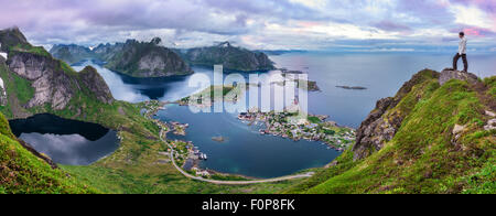 Escursionista maschio sulla cima di Mt. Reinebringen, isole Lofoten in Norvegia godendo della vista panoramica dopo il tramonto dal di sopra Foto Stock