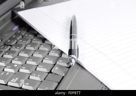 Blocco note e penna sulla tastiera di un computer portatile Foto Stock