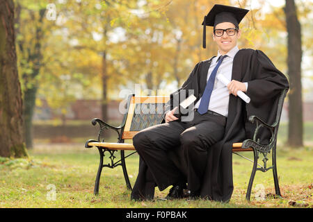 Studente laureato azienda diploma e un libro seduti su un banco di lavoro in posizione di parcheggio Foto Stock