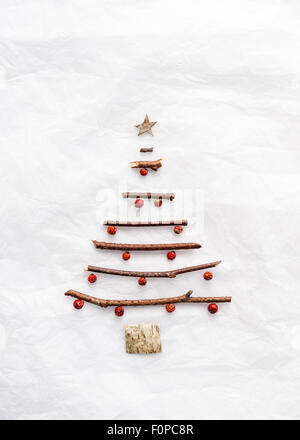 Un semplice albero di Natale forma resa con ramoscelli di corteccia di betulla e bacche rosse sulla carta velina bianca Foto Stock