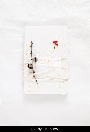 Regalo semplice involucro realizzato con carta velina bianca decorata con schizza di oro dipingere lo spago un ramoscello con pigne Foto Stock