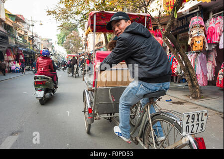 In rickshaw Hanoi, un conducente di un ciclo di risciò a Hanoi sguardi sulla sua spalla mentre dando un tour del vecchio quartiere, Vietnam Foto Stock