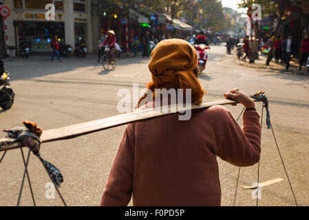 Donna vietnamita, vista posteriore di una donna che trasporta i suoi prodotti attraverso una strada nel quartiere vecchio di Hanoi, in Vietnam. Foto Stock