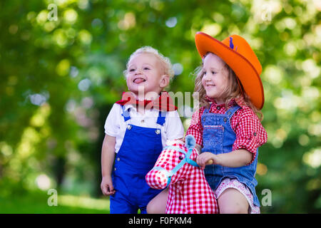 Piccolo Ragazzo e ragazza vestita come cowboy e cowgirl giocando con il giocattolo cavallo a dondolo nel parco. Bambini a giocare all'aperto Foto Stock