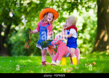 Piccolo Ragazzo e ragazza vestita come cowboy e cowgirl giocando con il giocattolo cavallo a dondolo nel parco. Bambini a giocare all'aperto Foto Stock