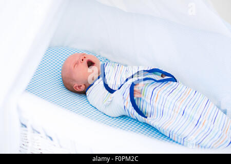 Adorabili neonato swaddled dorme nel letto bianco. Nuovo ragazzo nato tenendo un pisolino nel presepe blu. I bambini a dormire. La fasciatura per neonati. Foto Stock