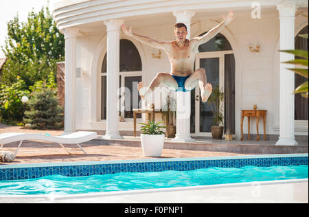 Felice giovane uomo salto in piscina Foto Stock