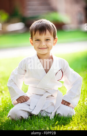 Sorridente little boy in kimono seduto sull'erba in posizione di parcheggio Foto Stock