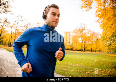 Giovane Uomo con cuffie in esecuzione in autunno la natura e ascolto di musica Foto Stock