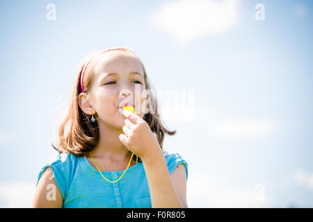 Cute girl teen insufflazione di fischio - blue sky in background Foto Stock