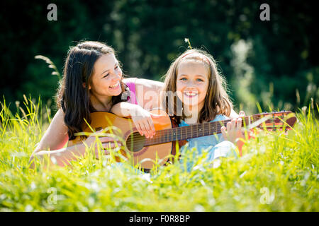 La Madre insegna chitarra plaing il suo bambino - outdoor in natura sulla giornata di sole Foto Stock