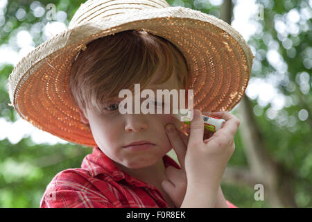 Triste ragazzo applicando il farmaco al suo pungiglione di insetto Foto Stock