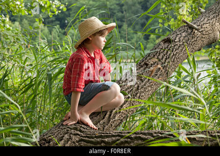 Ragazzo giovane vestito come Huckleberry Finn seduto in una struttura ad albero Foto Stock