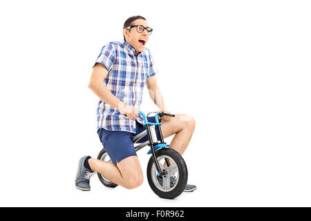 Studio shot di uno stupido ragazzo in sella ad una bicicletta minuscola isolati su sfondo bianco Foto Stock