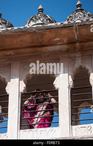 Jodhpur, India. Arenaria Mehrangarh hill fort di Marwar righelli. Una donna in Rajasthan rosa sari di guardare attraverso una finestra. Foto Stock