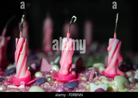 Rosa e Bianco swirly candeline di compleanno sulla parte superiore di una torta dopo essere stato bruciato, nel buio ma illuminata. Foto Stock
