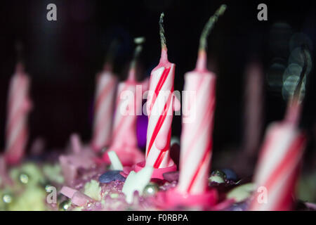 Rosa e Bianco swirly candeline di compleanno sulla parte superiore di una torta dopo essere stato bruciato, nel buio ma illuminata. Foto Stock