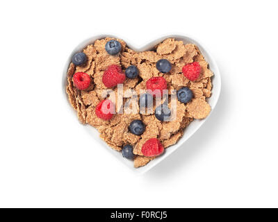 Colpo di cuore a forma di tazza di crusca di cereali con lamponi e mirtilli che implichi una sana alimentazione e stile di vita. L'immagine ha Foto Stock