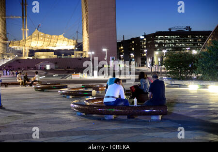 Le persone siedono sui banchi semicircolari in tarda serata sotto il grande arco a La Defense a Parigi. Foto Stock