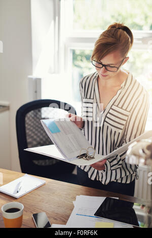 Giovane imprenditrice a lavorare a casa in piedi nel suo ufficio lettura delle note in un legante con un espressione seria Foto Stock