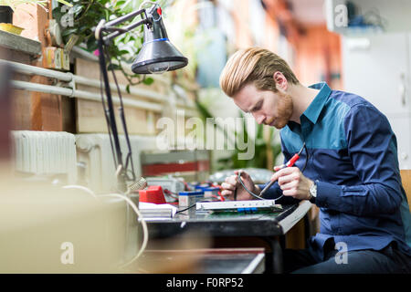 Giovane uomo bello la saldatura di una scheda a circuito stampato e lavorando sulla bulloneria di fissaggio Foto Stock