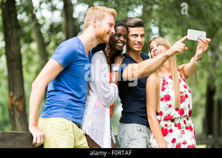 Un gruppo di giovani e coppie tenendo selfies nella natura e sorridente Foto Stock