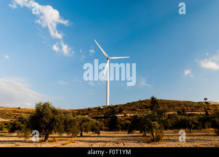 Turbine a vento sulla collina di ulivi, cielo blu e nuvole come sfondo. La modalità Eco power. Foto Stock