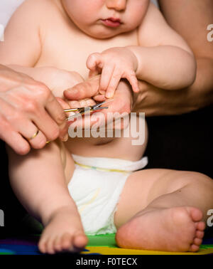 Madre il taglio di unghie delle mani del suo bambino - seduta sul pavimento nel bagno Foto Stock