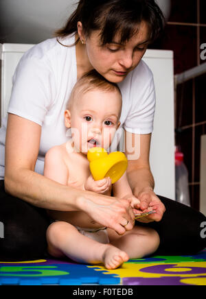 Madre il taglio di unghie di suo figlio mentre il bambino sta giocando con i giocattoli Foto Stock