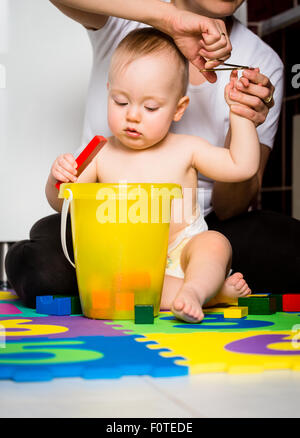 Madre il taglio di unghie di suo figlio mentre il bambino sta giocando con i giocattoli Foto Stock