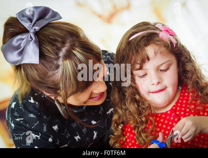 Madre aiutare bambina tagliare con le forbici Foto Stock