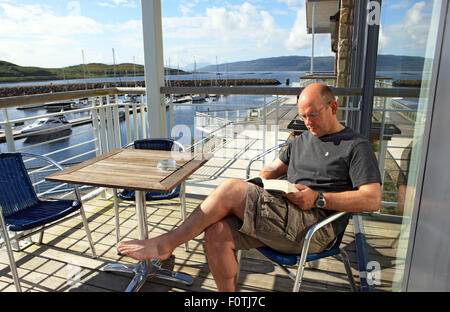 L'uomo rilassarsi leggendo un libro su un balcone a Portavadie Marina in Scozia su Loch Fyne Foto Stock