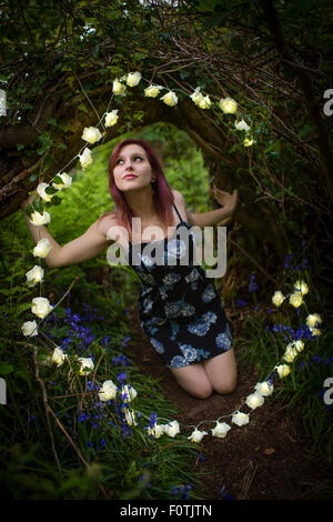 Fantasie da favola: una giovane donna ragazza adolescente da solo da se stessa inginocchiati indossa un abito nel bosco circondata da una ghirlanda di fiori bianchi luci, serata estiva REGNO UNITO Foto Stock