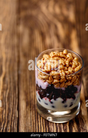 Parfait di stile a più livelli sani snack o dessert con yogurt,mirtillo,marmellata di mirtilli freschi,miele soffiato il frumento in vetro su legno Foto Stock