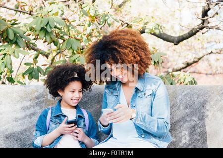 Madre e figlia seduti fianco a fianco guardando sorridendo gli smartphone Foto Stock