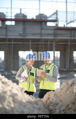 Geometra con tavoletta digitale parlando di builder sul sito in costruzione Foto Stock