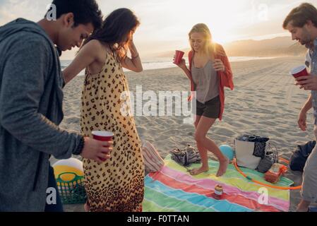 Gruppo di amici avente party sulla spiaggia al tramonto Foto Stock