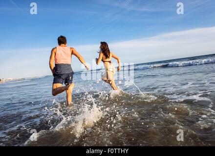 Coppia giovane in esecuzione in mare, vista posteriore Foto Stock