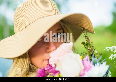 Close up ritratto di giovane donna con il mazzo di fiori e indossando cappello di paglia Foto Stock