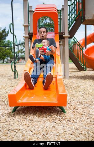 Giovane uomo lo scorrimento verso il basso con il toddler fratello sul parco giochi slitta Foto Stock