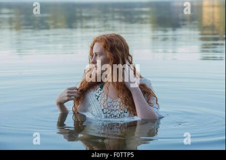 La testa e le spalle del giovane donna con lunghi capelli rossi nel lago guardando lateralmente Foto Stock