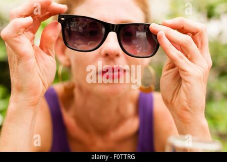 Metà donna adulta holding occhiali da sole di fronte ai suoi occhi Foto Stock