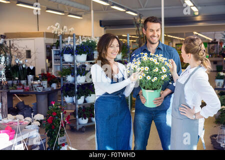 Fioristi assistendo il cliente maschio nell' acquisto di piante di fiori Foto Stock