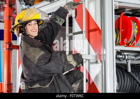 Firefighter sorridente in piedi sul carrello nella stazione dei vigili del fuoco Foto Stock