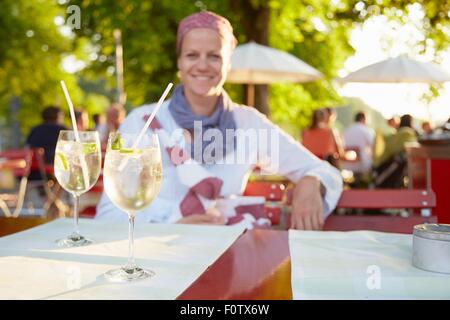 Donna matura, all'aperto, seduta a tavola con bevande Foto Stock