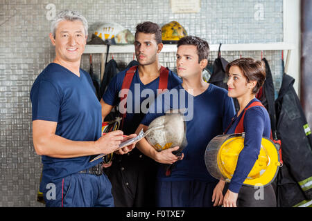 Felice vigile del fuoco in piedi con il team presso la stazione dei vigili del fuoco Foto Stock