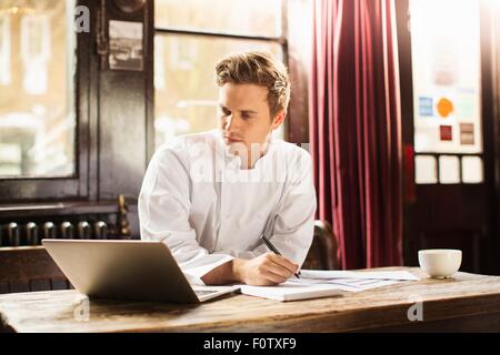 Giovane uomo che indossa lo chef uniforme utilizzando laptop Foto Stock