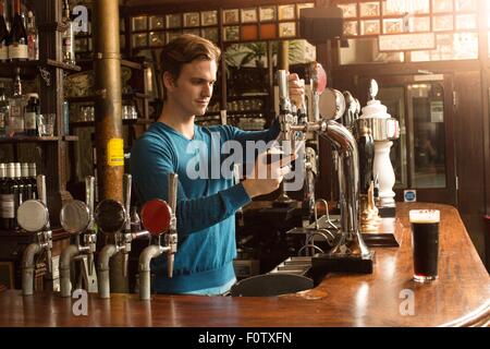 Giovane uomo che lavora in public house, che serve bevande Foto Stock