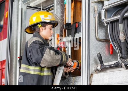 Firefighter femmina che fissa il tubo flessibile di acqua nel carrello Foto Stock