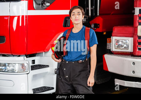 Fiducioso firewoman holding casco contro firetruck Foto Stock